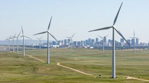 Turbine eoliene pe un câmp verde, cu oraș în fundal.